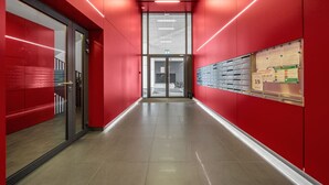A corridor with red walls, glass doors, and a row of lockers on the right. - Kasprzaka 29C - Terrace, Workspace, EXPO - by Rentujemy (Warszawa)