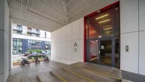 A modern building entrance with a glass door, a staircase leading to the entrance, and bicycles parked outside. - Kasprzaka 29C - Terrace, Workspace, EXPO - by Rentujemy (Warszawa)