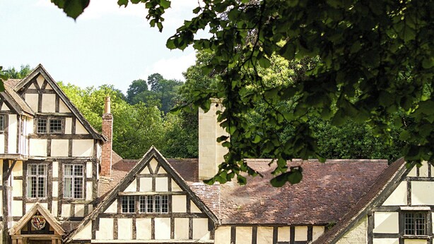 Un bâtiment traditionnel à colombages, doté d’une cheminée centrale imposante, de nombreuses fenêtres et d’une entrée en pierre.