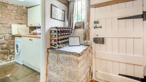Une cuisine rustique avec des murs en pierre, des poutres en bois, un lave-linge et un meuble à vin.