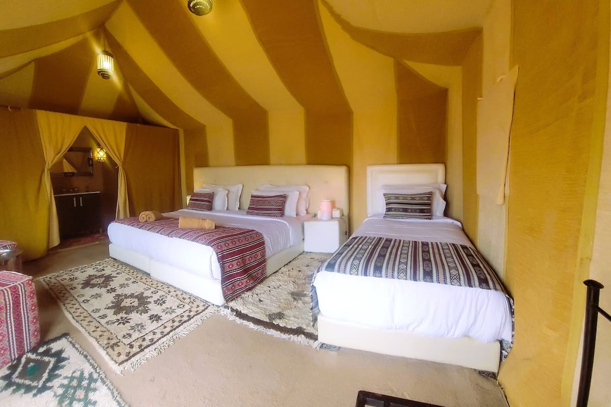 A cozy tent-style room with two beds, a small table, and a decorative rug.