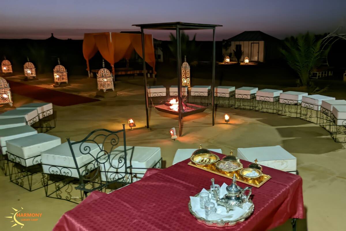 An outdoor dining area with a red tablecloth, white chairs, and a central fire feature.