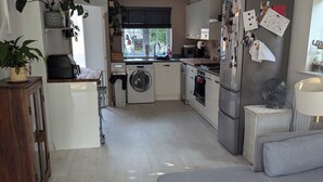 A compact kitchen with a washing machine, a refrigerator, and a dining area with a table and chairs. - Tranquil Wells Retreat (Wells)