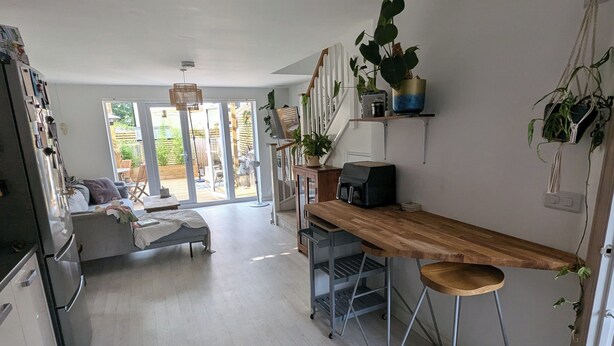 A modern kitchen with a wooden countertop, bar stools, and a coffee machine. There is a sliding glass door leading to a patio area with outdoor furniture. - Tranquil Wells Retreat (Wells)