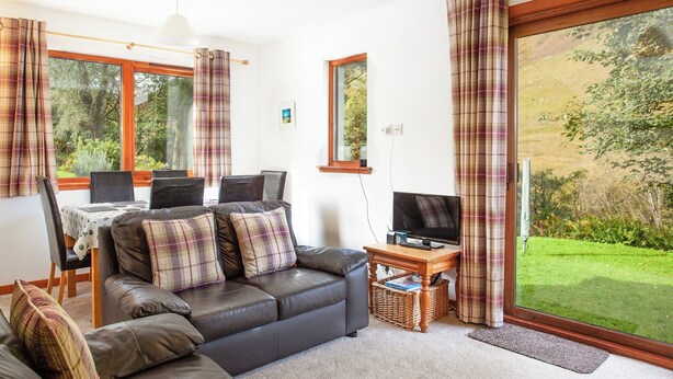 A cozy living room with a sofa, a dining table, and a TV. - Bidean Cottage - UK41933 (Glencoe)