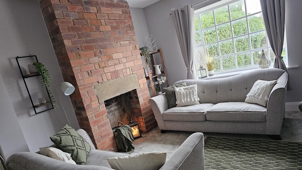 A living room with a brick fireplace, a grey sofa, and a green rug. - The Sweetbriar Cottage 3 Bedroom House in Leeds (Leeds)