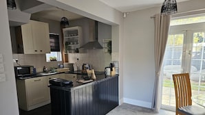 A compact kitchen with a central island, built-in appliances, and a dining area with a view. - The Sweetbriar Cottage 3 Bedroom House in Leeds (Leeds)