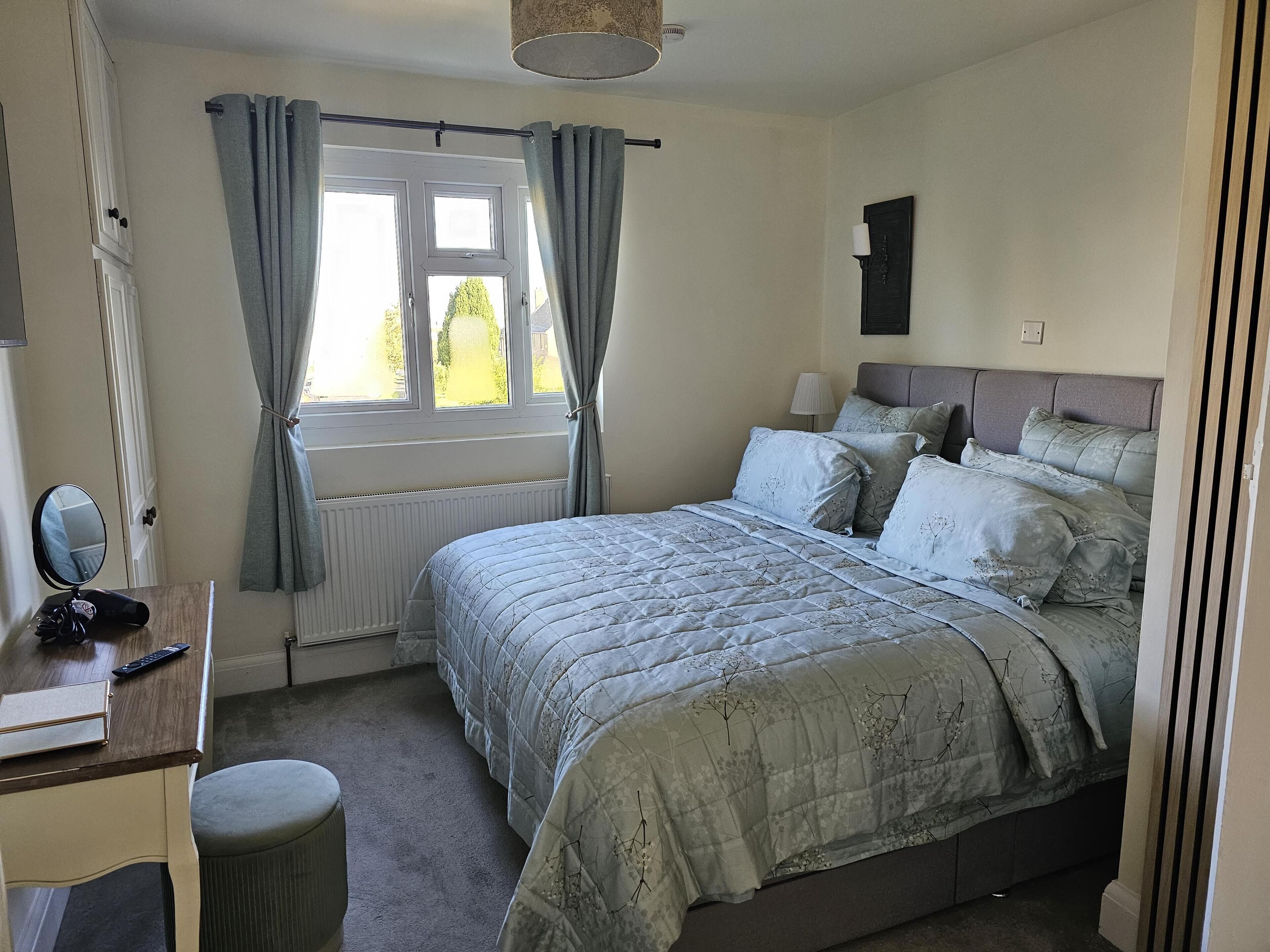 Une chambre à coucher avec un lit, une table de chevet, une lampe et une fenêtre avec des rideaux.