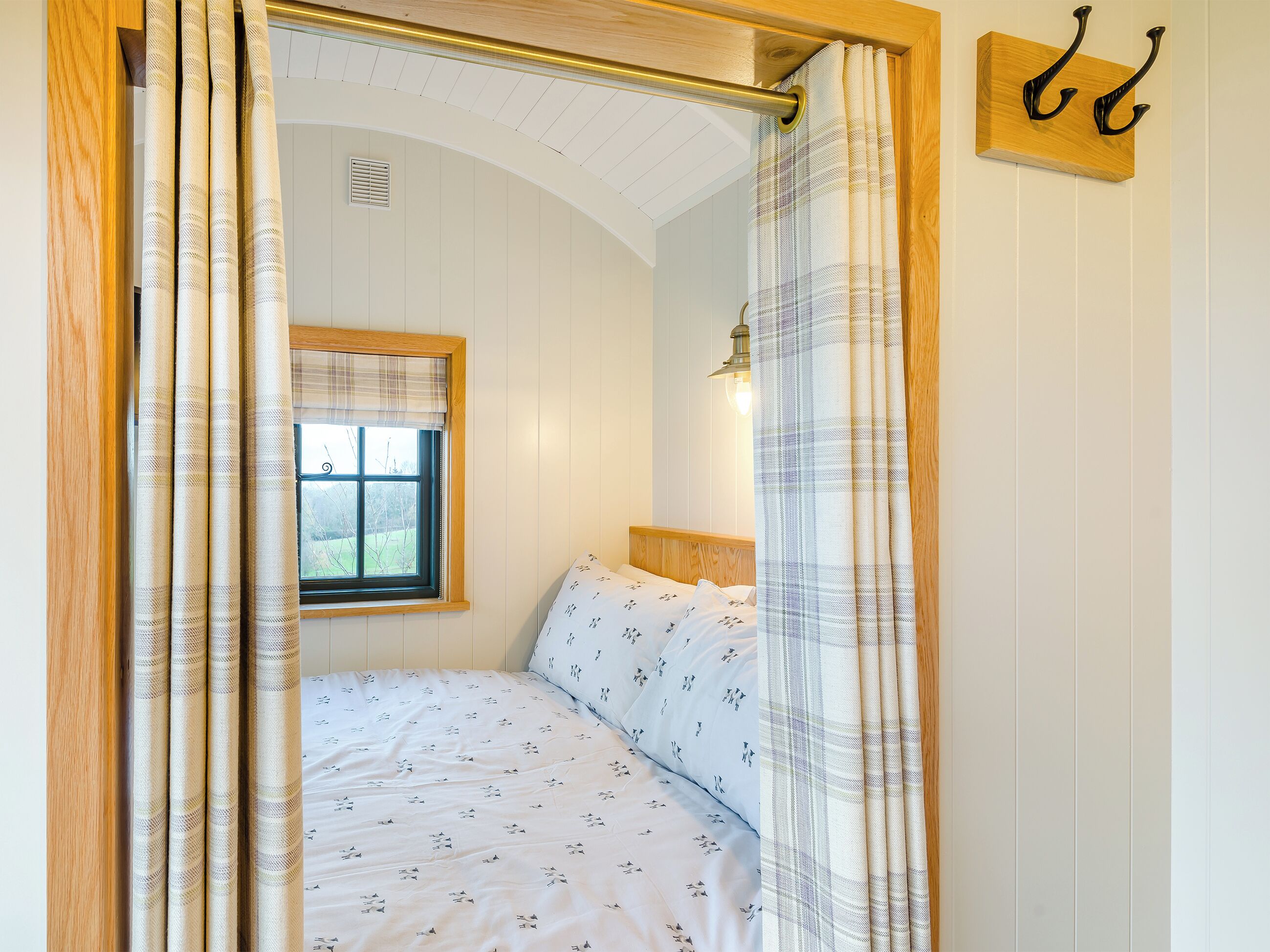 Ein Schlafzimmer mit Bett, Fenster, Wandleuchte und einem hölzernen Kopfteil.