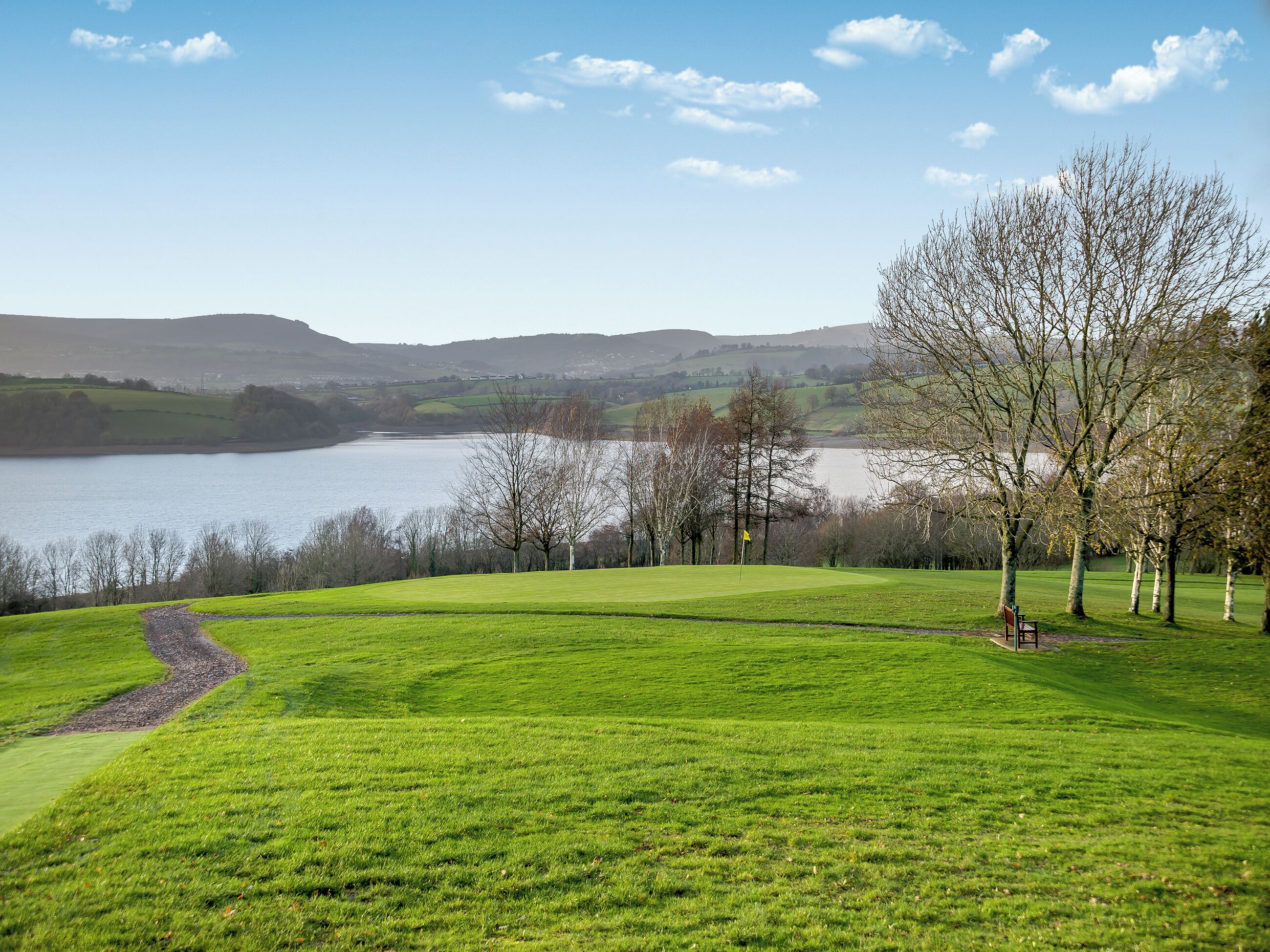 A grassy field with a lake and hills in the background.