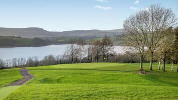 A grassy field with a lake and hills in the background.