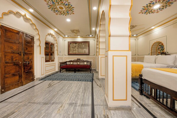 A room with a marble floor, wooden doors, a bed with a yellow bedspread, and a red sofa. - Raghunath Haveli - A Heritage Homestay (Jaipur)