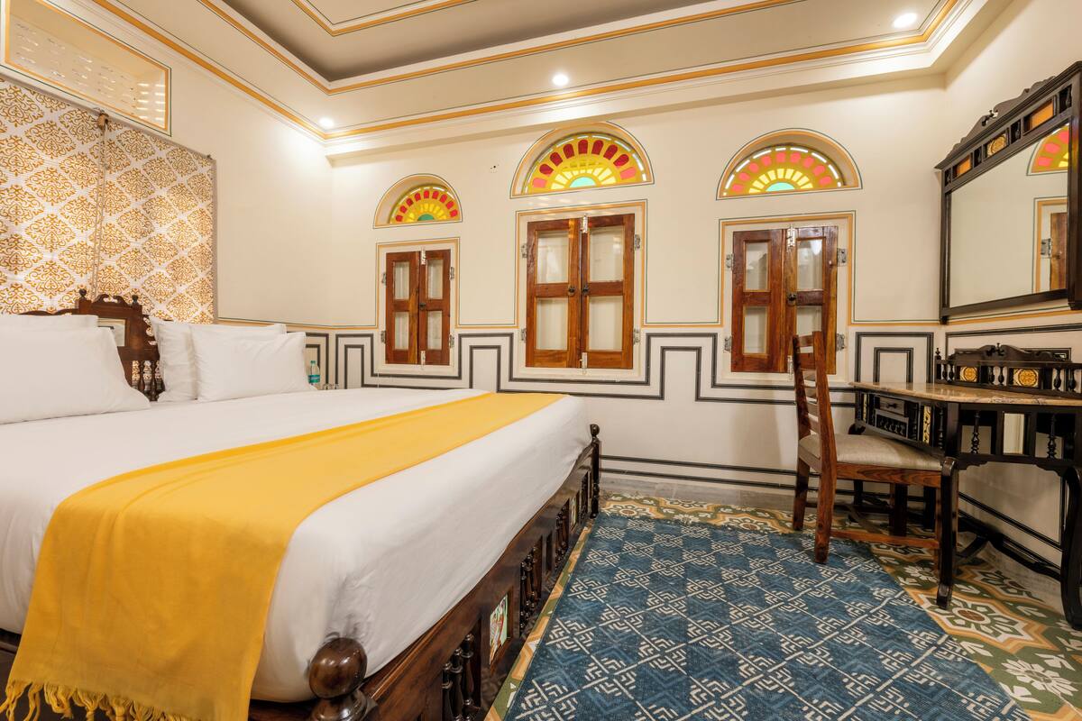 Une chambre d’hôtel avec un grand lit, une chaise en bois, un bureau et des panneaux décoratifs sur les murs.