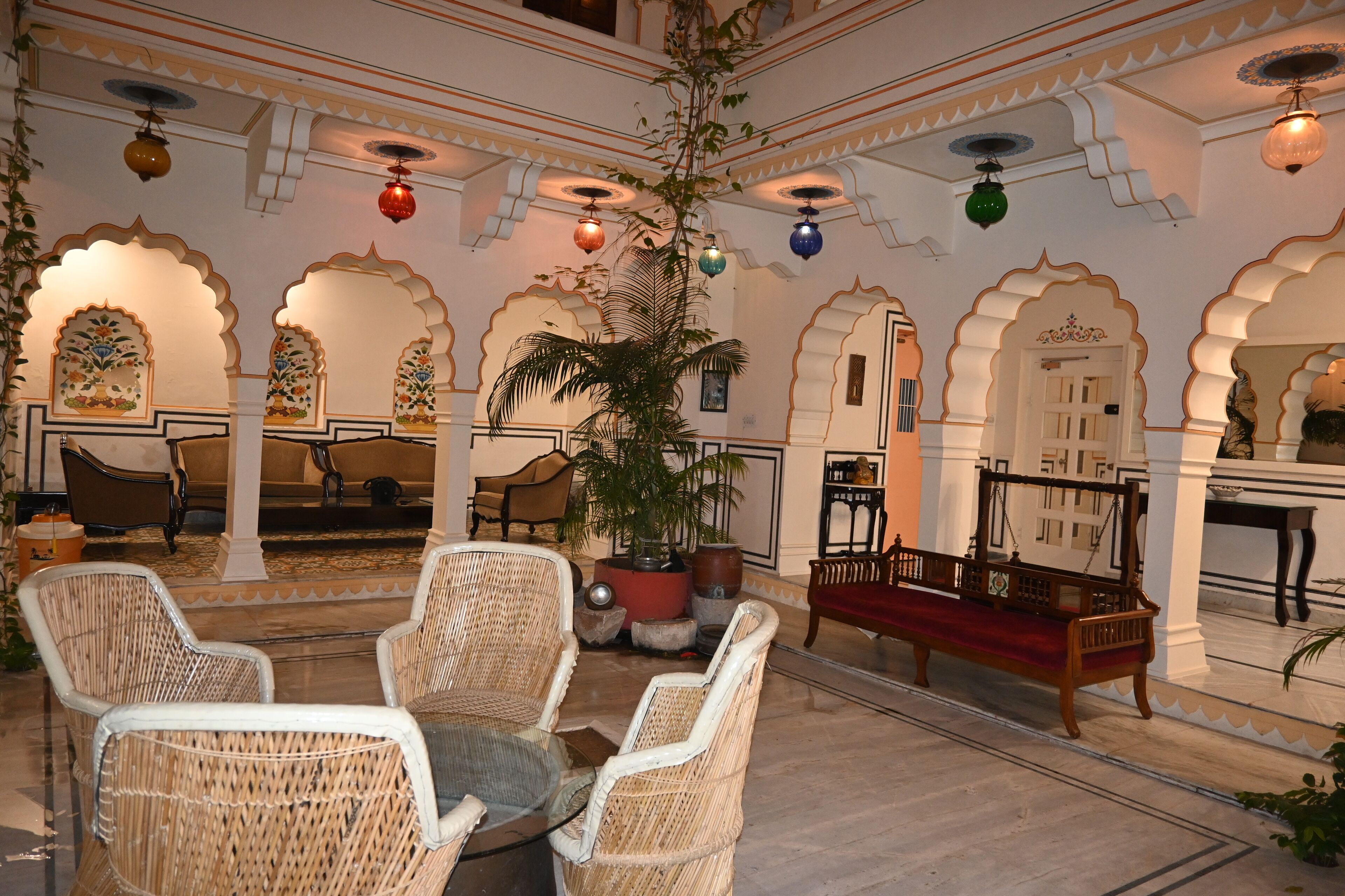 A traditional interior with wicker furniture, a central potted plant, and ornate arches.