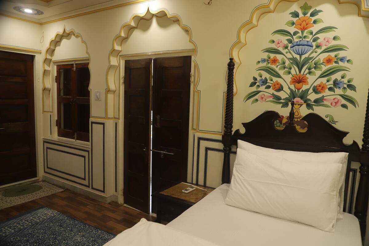 Une pièce avec un lit, une porte en bois et un mur orné d’une fresque florale.