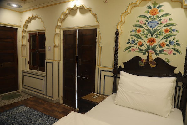 A room with a bed, a wooden door, and a wall with a floral mural. - Raghunath Haveli - A Heritage Homestay (Jaipur)