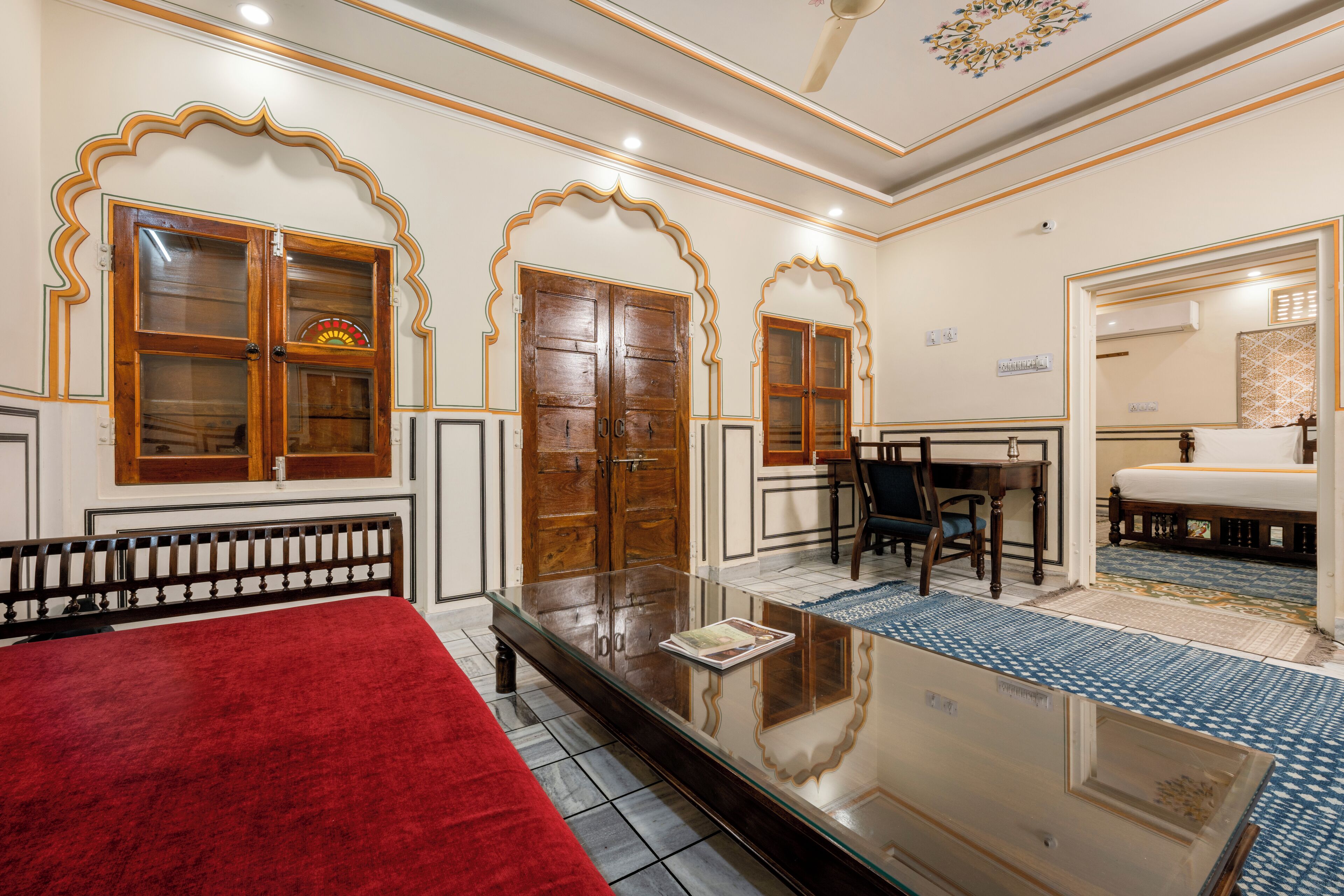 A traditional room with a bed, a glass-top table, and a desk with a chair.