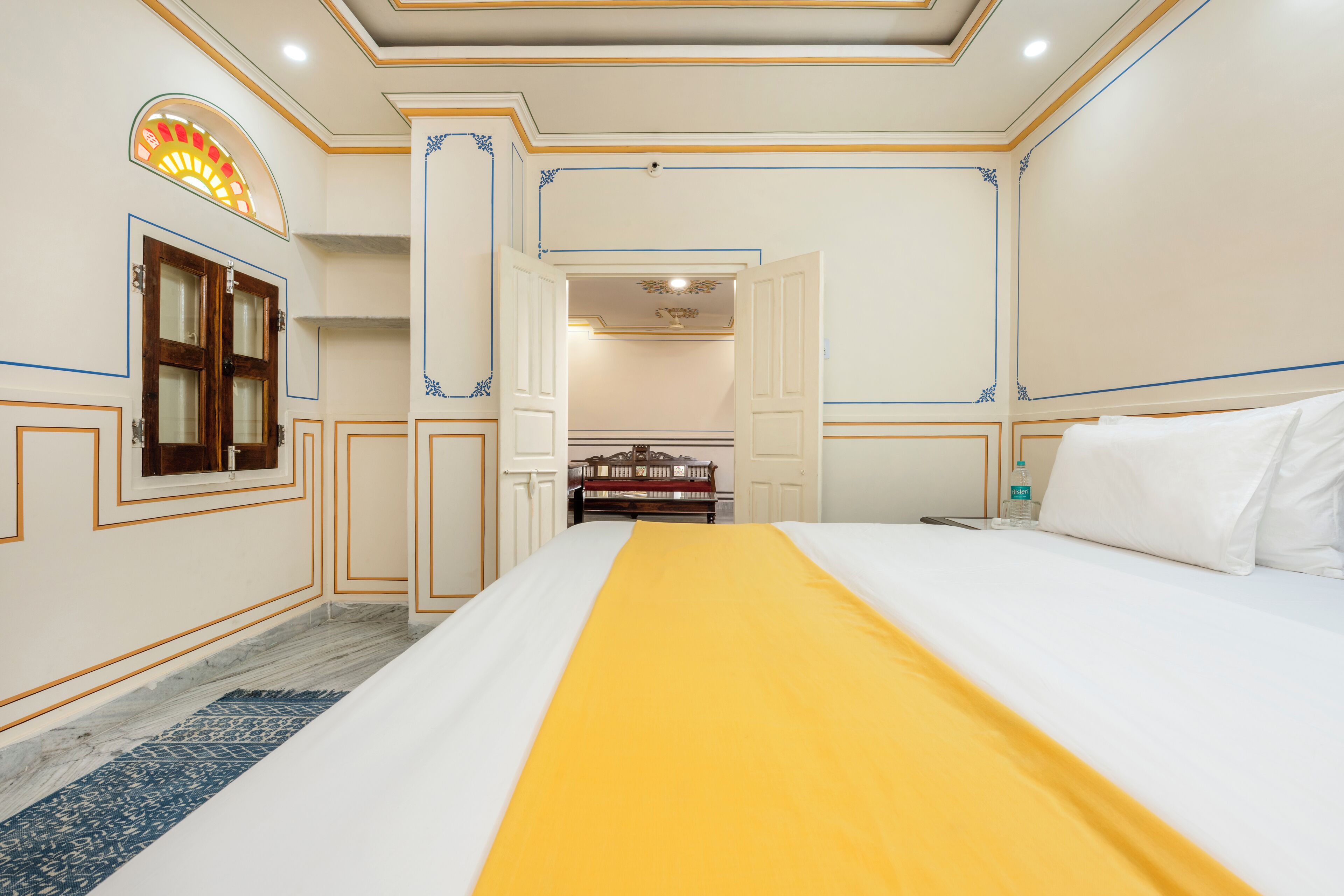 Een hotelkamer met een groot bed, een houten garderobe, een klein tafeltje en een spiegel.
