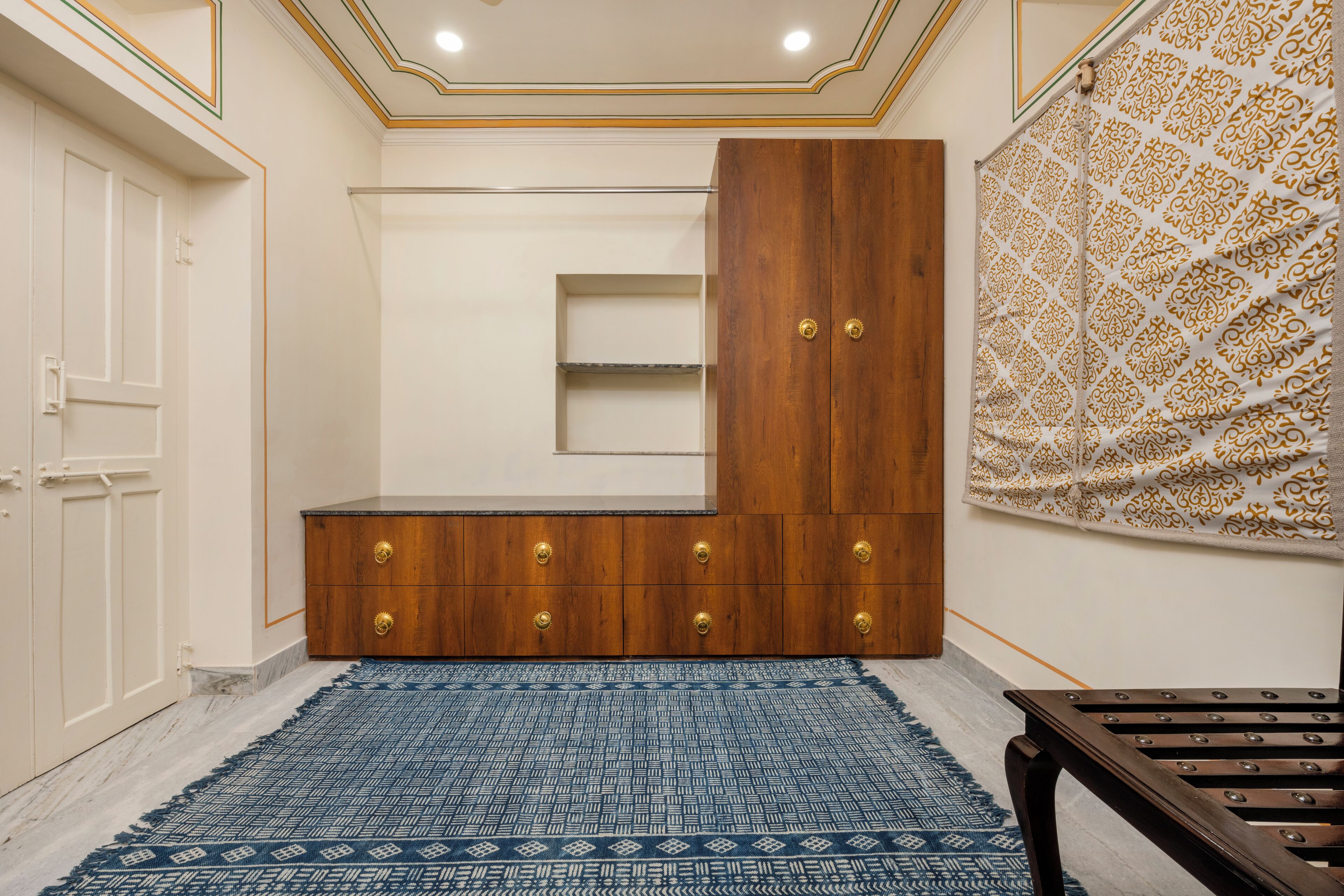 A room with a wooden cabinet, a blue patterned rug, and a patterned wall hanging.
