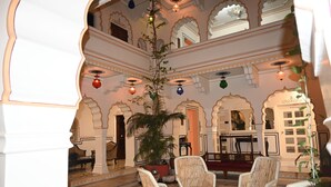Ein traditionelles Interieur mit einem runden Glastisch, umgeben von Korbstühlen, einer großen Topfpflanze und verzierten Bögen.