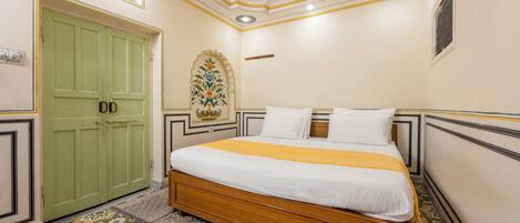 A bedroom with a wooden bed, a green door, patterned floor, and decorative ceiling.