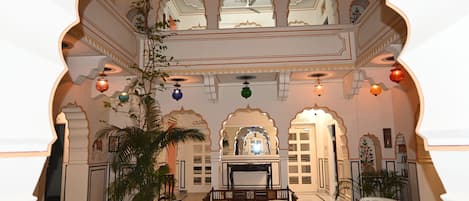 Un interior decorado al estilo tradicional indio, con arcos ornamentales, una zona de estar central y elementos decorativos colgantes.