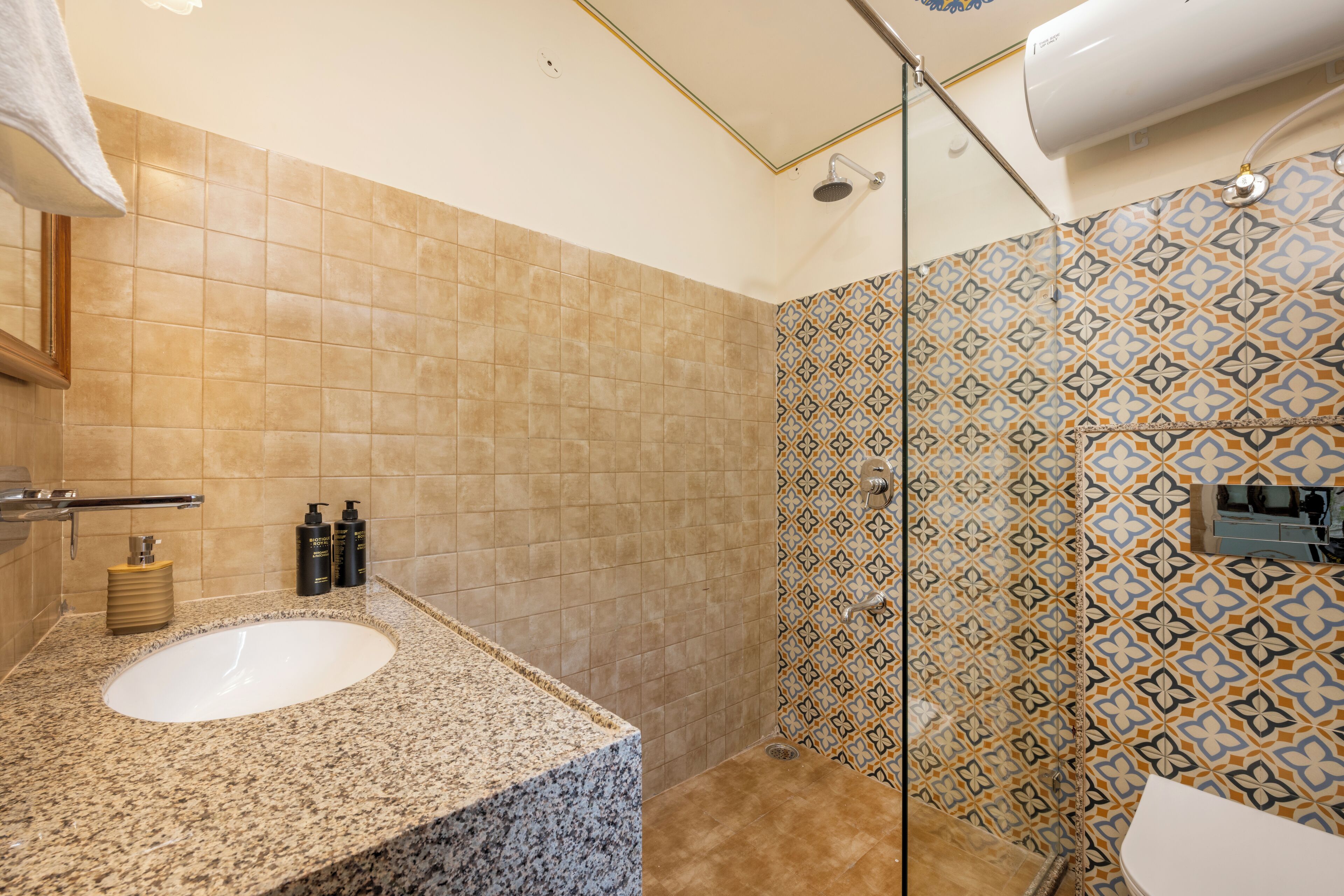Een badkamer met een wastafel met granieten blad, een douche met glazen deur en behangtegels op de muren.