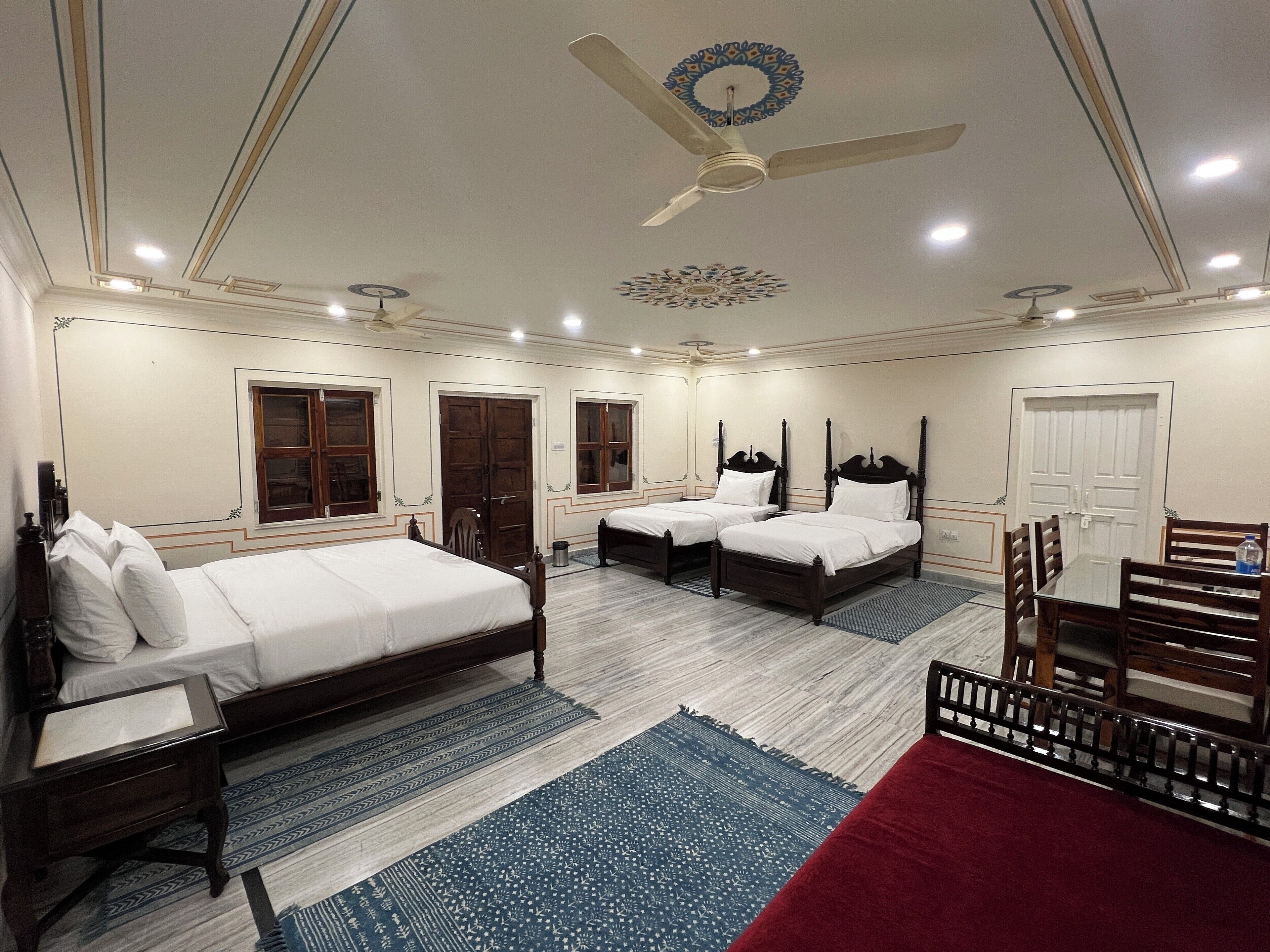 A hotel room with two beds, a ceiling fan, and a dining table with chairs.