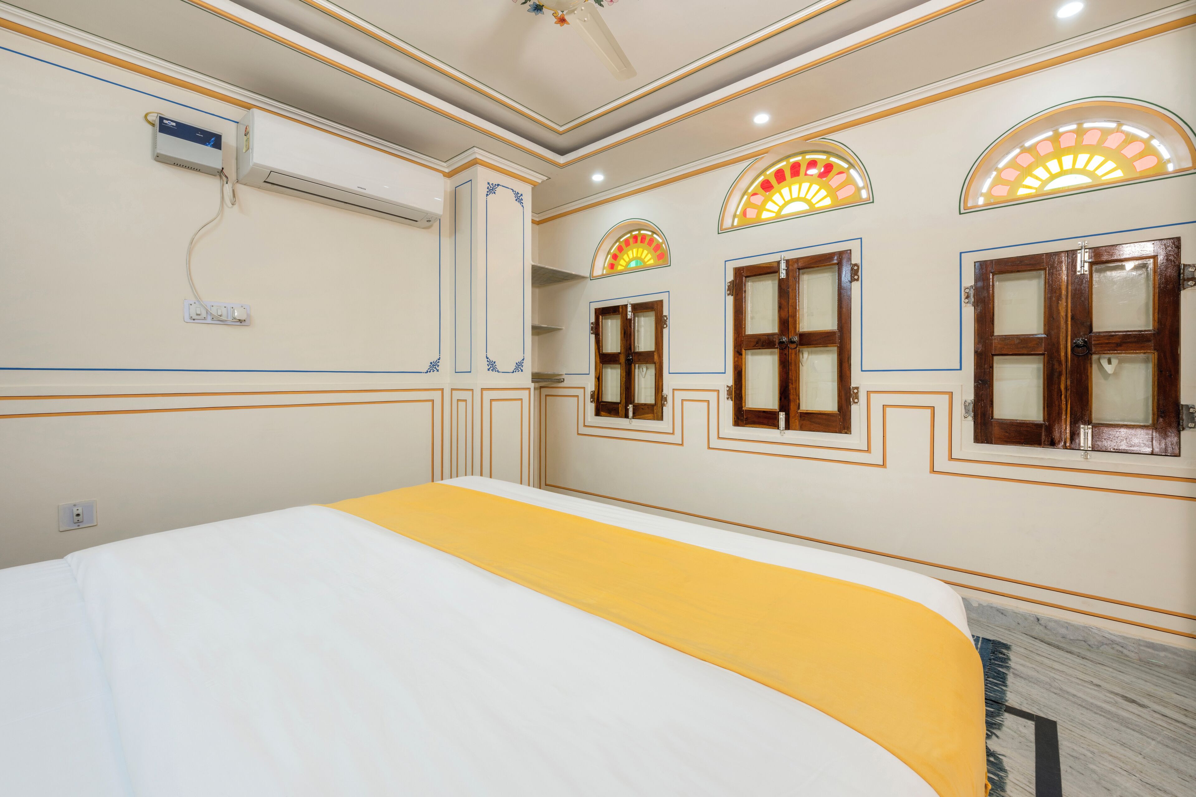 A hotel room with a bed, an air conditioning unit, and decorative wall sconces.