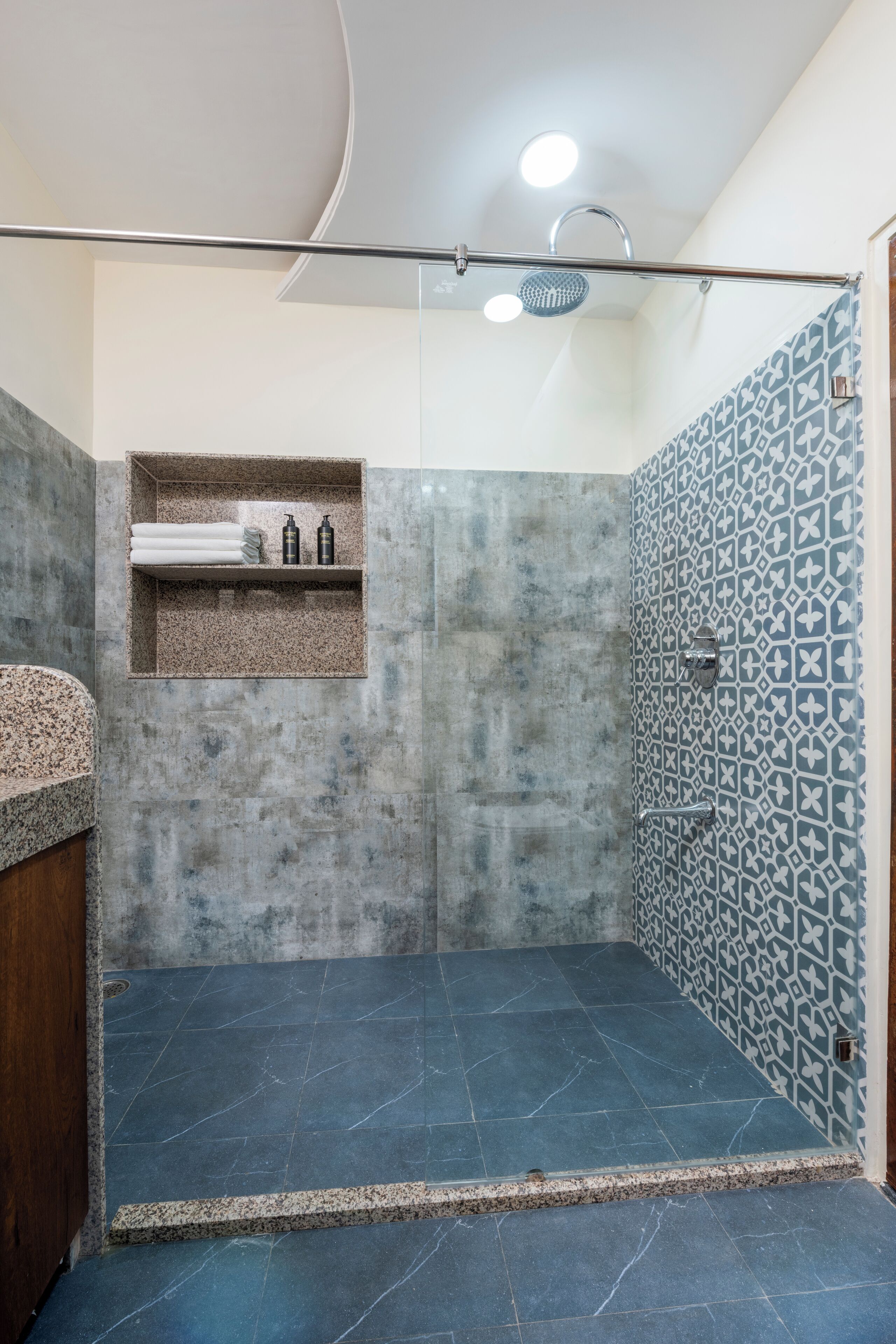 A modern bathroom with a shower area, a built-in shelf with toiletries, and a patterned tile wall.