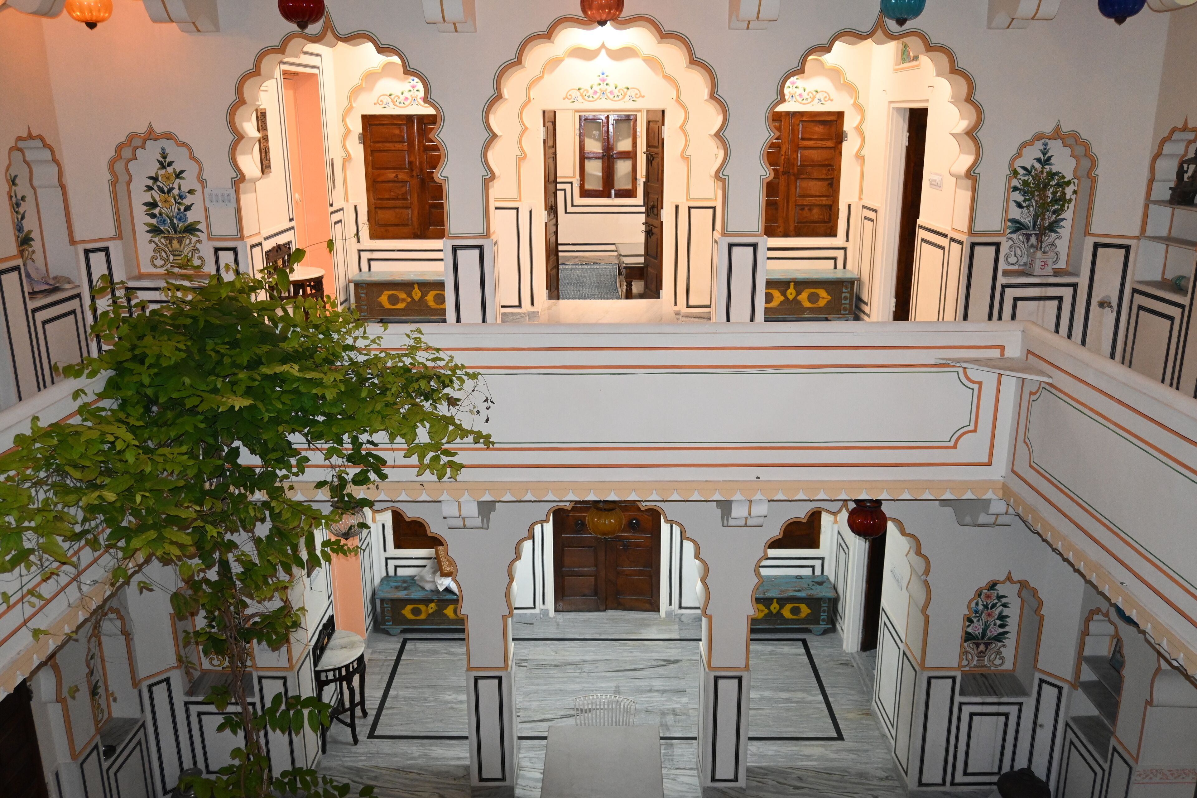 A traditional Indian courtyard with ornate arches, a central seating area, and a tree in the foreground.
