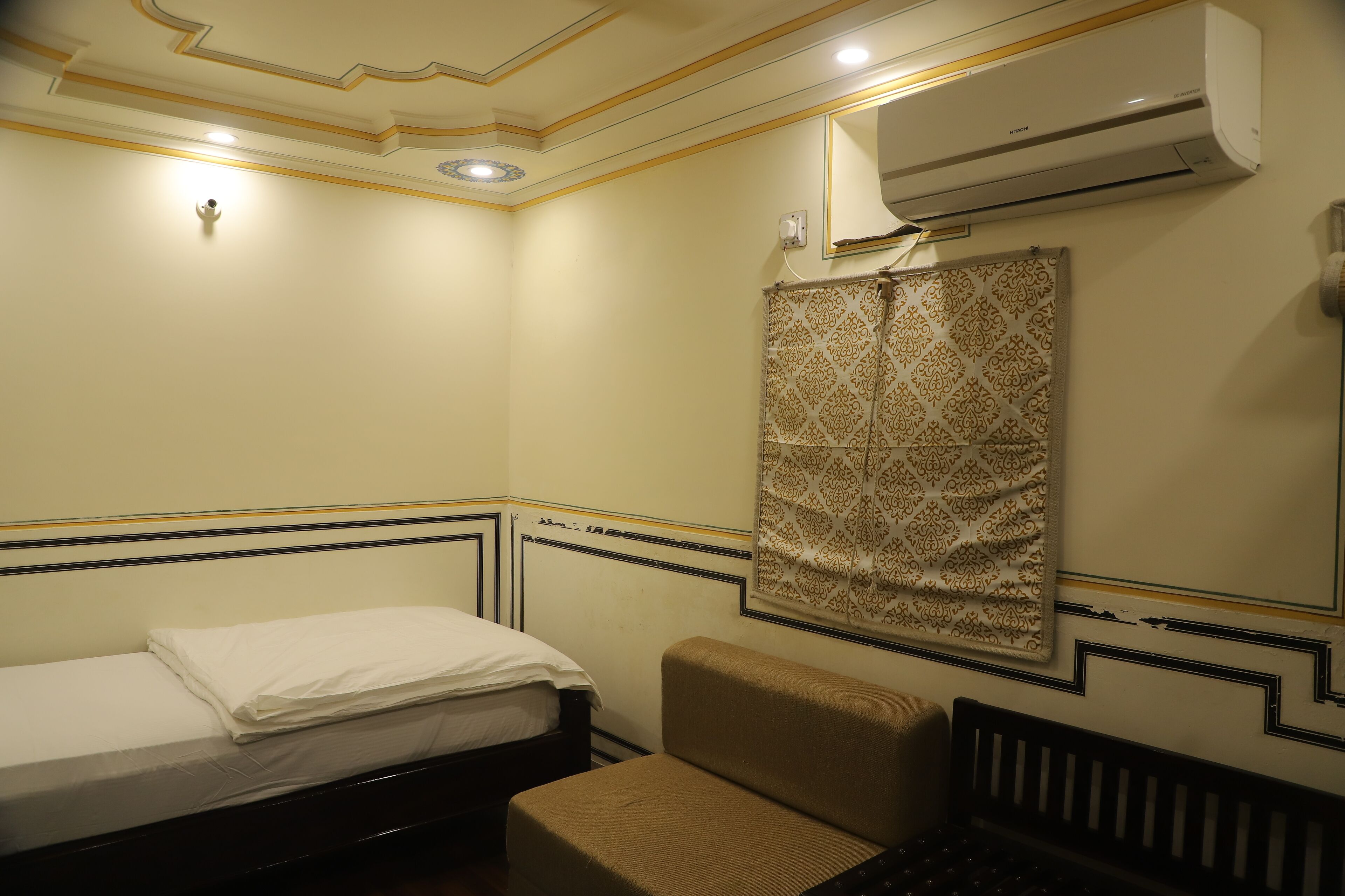 Una habitación pequeña y ordenada con una cama, un banco y una cortina estampada.