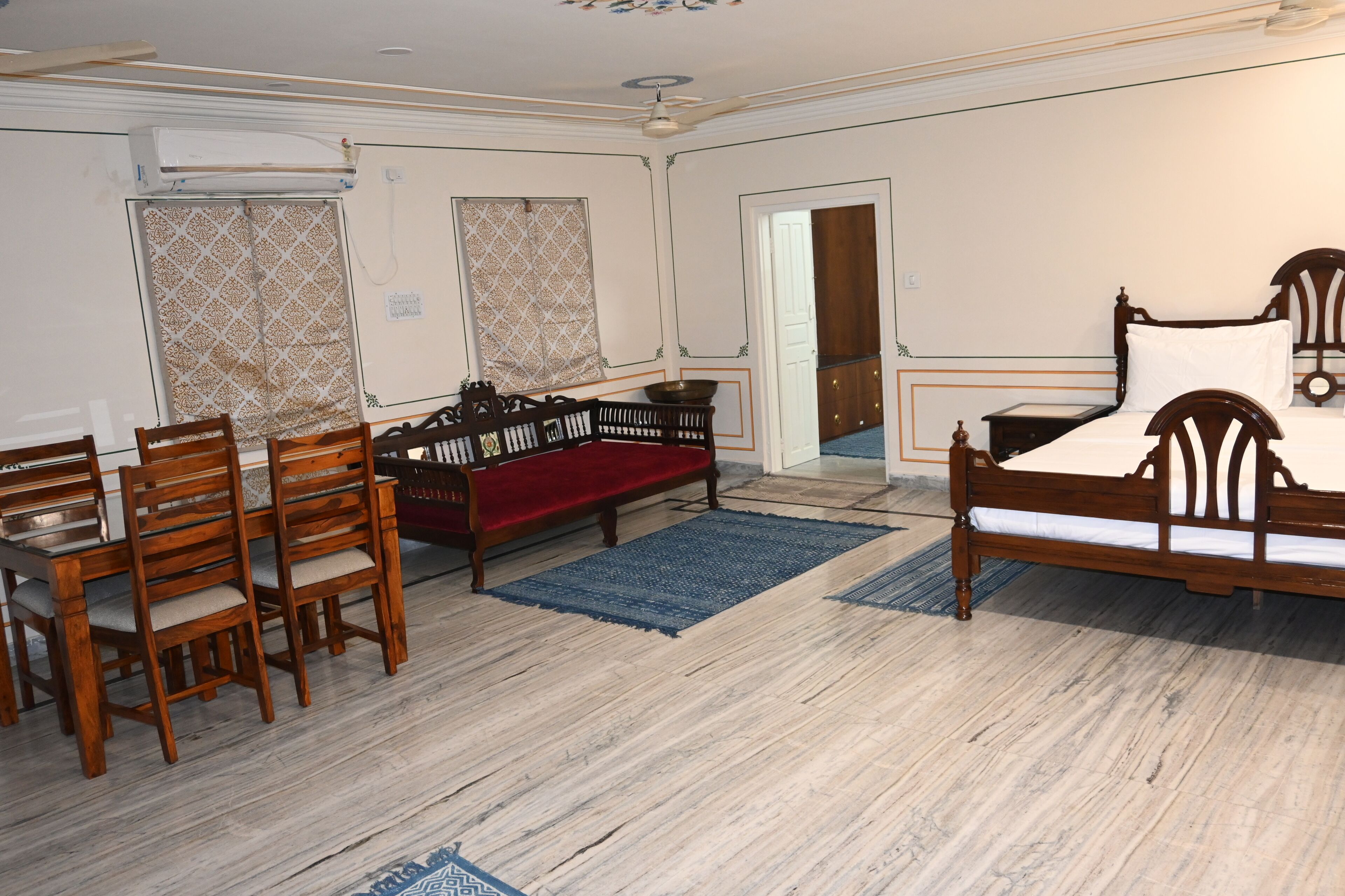A room with a wooden bed, a red sofa, a dining table with chairs, and a blue rug.
