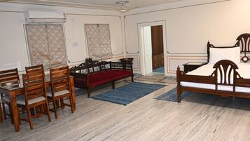 A room with a wooden bed, a red sofa, a dining table with chairs, and a blue rug.