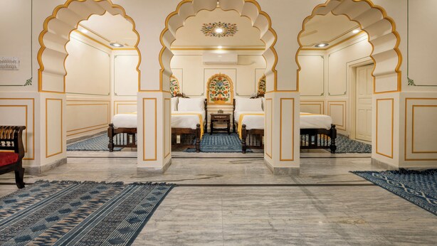 Ein Hotelzimmer im traditionellen Stil mit einem zentral platzierten Bett, das von zwei Sofas, einem kleinen Tisch und einem dekorativen Spiegel flankiert wird.