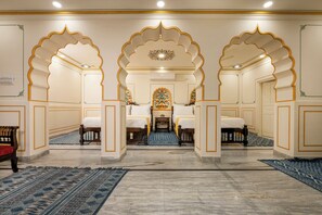 A hotel room with a traditional design, featuring a central bed flanked by two sofas, a small table, and a decorative mirror. - Raghunath Haveli - A Heritage Homestay (Jaipur)