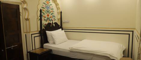 A room with a bed, a wooden nightstand, a door, and a wall with a floral design.