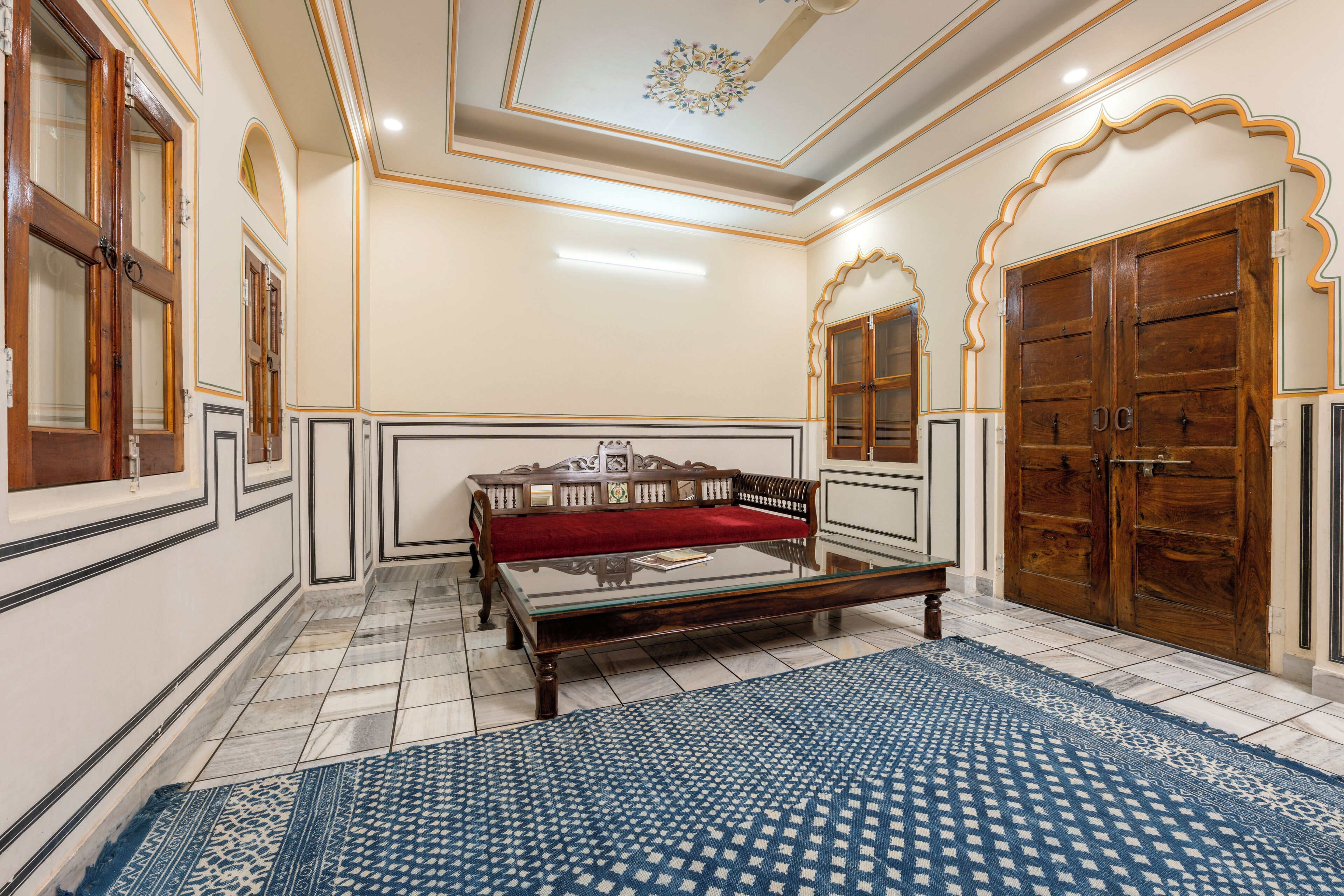 A room with a glass-top table, a red sofa, and a patterned rug.