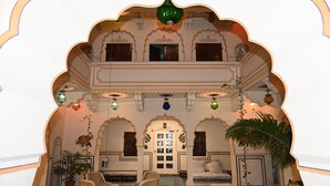 Ein traditioneller Palast in Indien, innen mit aufwendigen Bögen, einer zentralen, mehrteiligen Tür und Sitzbereichen mit Kissen.