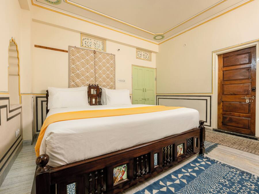 Un dormitorio ordenado con una cama, una puerta verde y un papel tapiz estampado.
