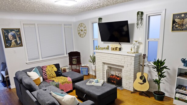 A living room with a grey sofa, a fireplace, a flat-screen TV, and a guitar. - Pretty home in the heart of Edmonton. Main floor, Pet-Friendly! (Edmonton)
