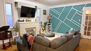A living room with a fireplace, a sofa, a television, and a guitar. - Pretty home in the heart of Edmonton. Main floor, Pet-Friendly! (Edmonton)