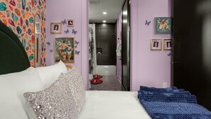 A bedroom with a bed, a bathroom visible through an open door, and a refrigerator.