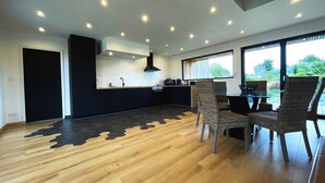 A modern kitchen with a black countertop, a built-in stove, and a black range hood. There is a dining area with wicker chairs and a table. The floor has a unique black and brown pattern. - house Porzh Loaz. (Plouha)