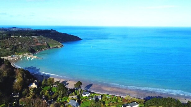 A coastal landscape with a beach, clear blue sea, and a small settlement with houses and boats. - house Porzh Loaz. (Plouha)