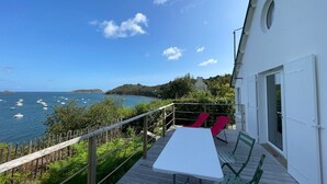 A balcony with a white table and two red chairs overlooking a coastal area with boats and greenery. - Ty Lazo: Serenity by the sea, haven of peace. (Plouézec)