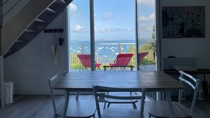 A spacious room with a large sliding glass door leading to a balcony with red chairs and a view of the sea. - Ty Lazo: Serenity by the sea, haven of peace. (Plouézec)