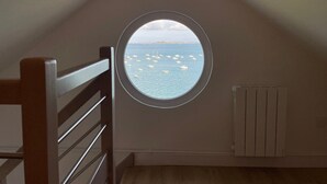 A room with a sloped ceiling and a window overlooking a body of water with boats. - Ty Lazo: Serenity by the sea, haven of peace. (Plouézec)