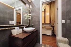 A bathroom with a large mirror, a white sink, and a decorative vase with flowers. - Imperial - Luxury Grand Opening (Roma)