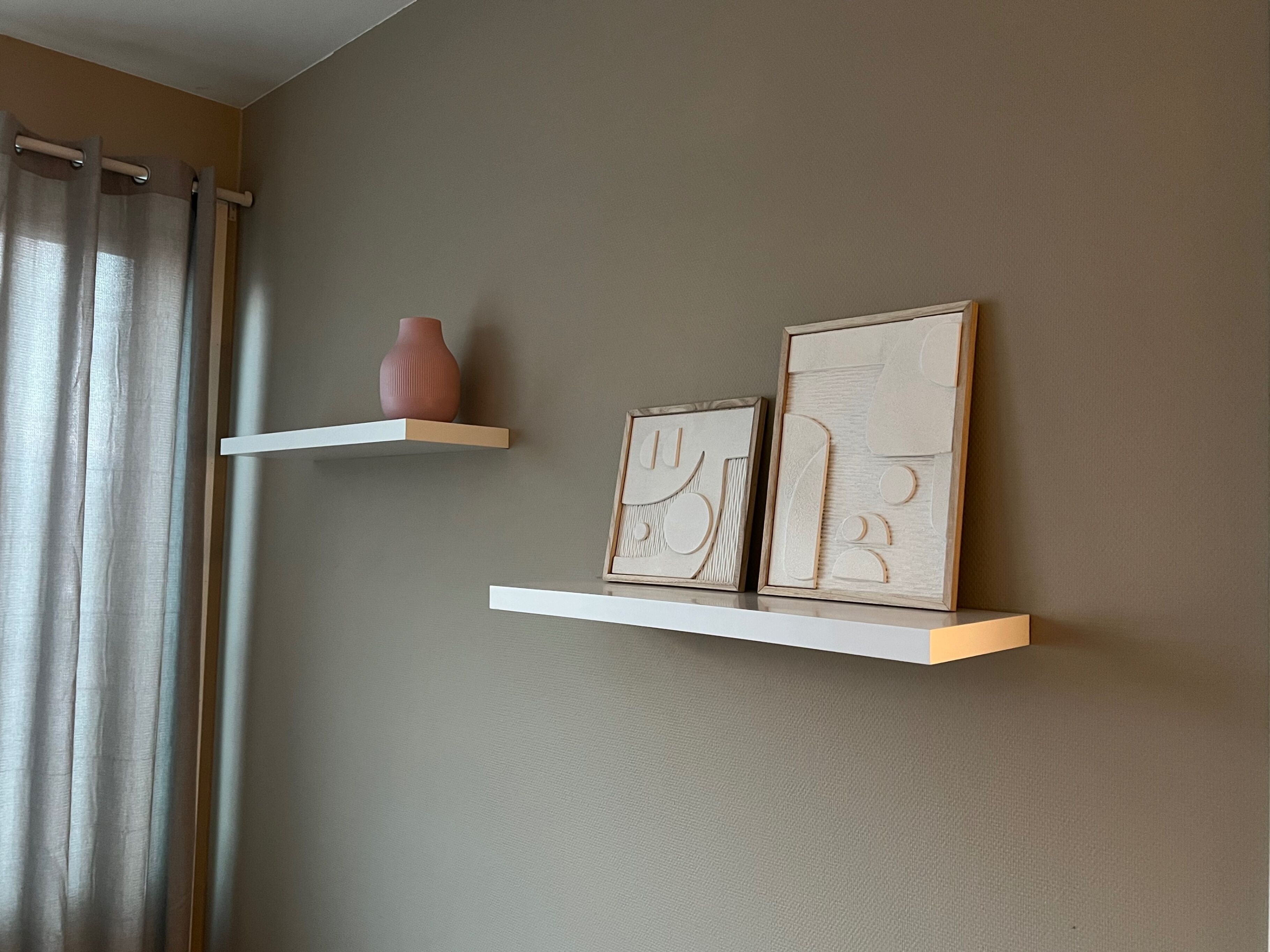 A room with two white floating shelves, one holding a vase and the other with framed artwork.